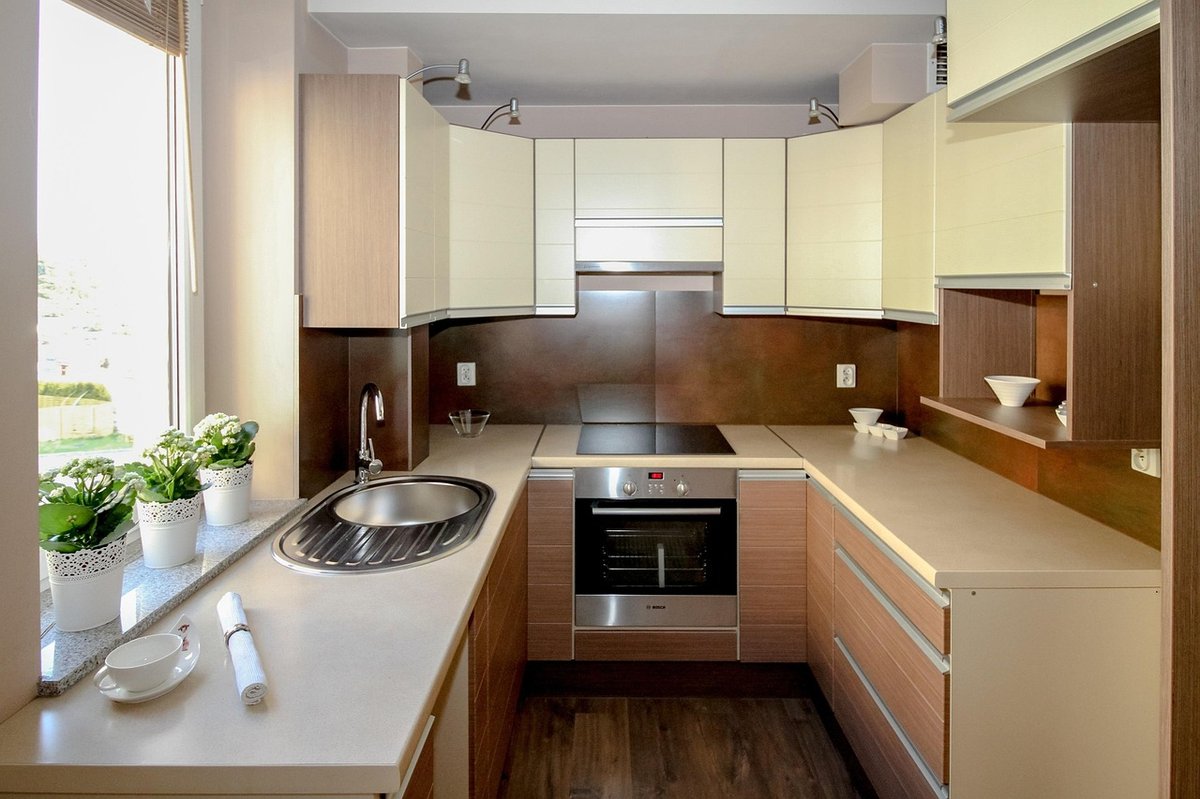 Compact fitted kitchen with cream cabinets, a built-in oven and a window-side sink